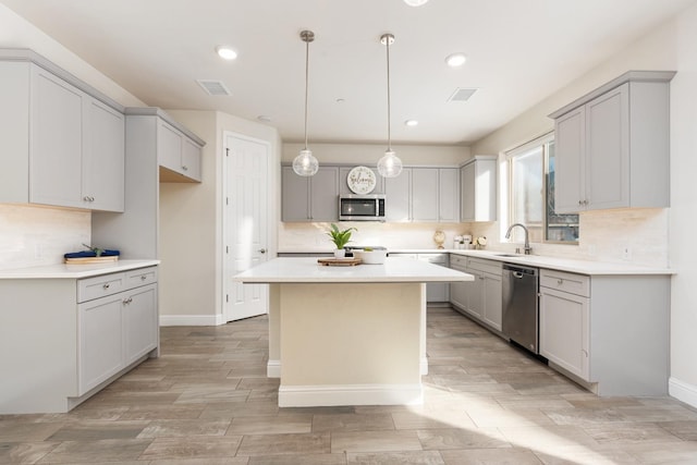 kitchen with appliances with stainless steel finishes, decorative light fixtures, sink, gray cabinetry, and a center island