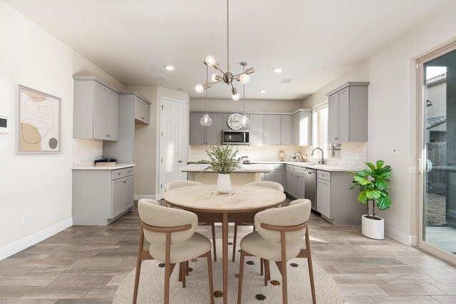 kitchen featuring gray cabinets, appliances with stainless steel finishes, backsplash, hanging light fixtures, and a notable chandelier