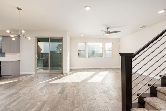 unfurnished living room featuring ceiling fan with notable chandelier