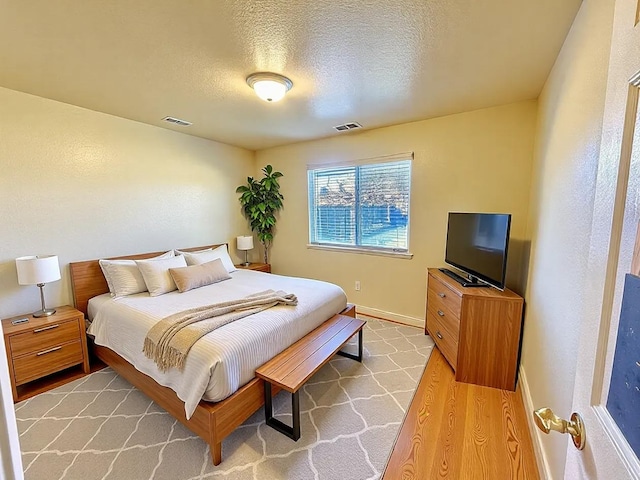 bedroom with light wood-style floors, baseboards, visible vents, and a textured ceiling