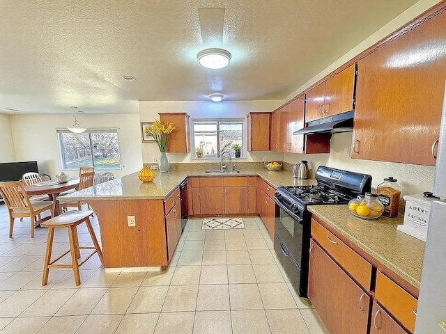 kitchen featuring brown cabinets, a peninsula, under cabinet range hood, black appliances, and a sink