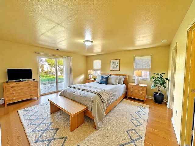 bedroom featuring baseboards, access to outside, a textured ceiling, and light wood-style floors