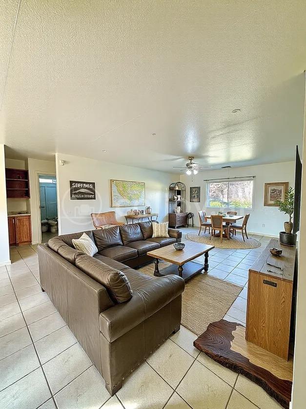 living area with a ceiling fan, a textured ceiling, and light tile patterned flooring