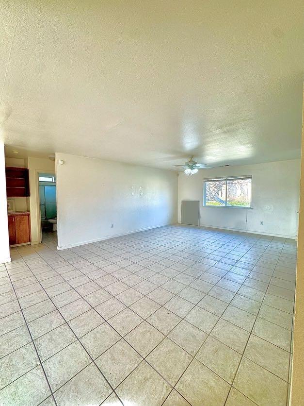 empty room with ceiling fan, a textured ceiling, and light tile patterned floors