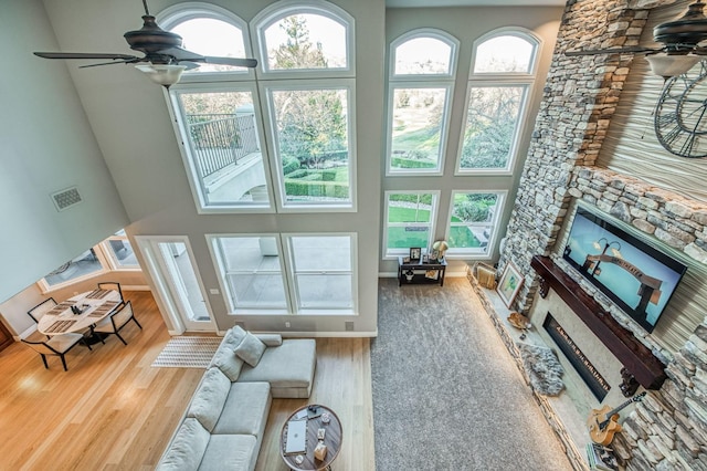 living room with a stone fireplace, a towering ceiling, ceiling fan, and hardwood / wood-style flooring