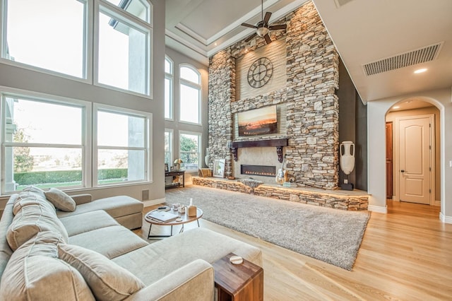 living room with a towering ceiling, a healthy amount of sunlight, a stone fireplace, and light hardwood / wood-style floors