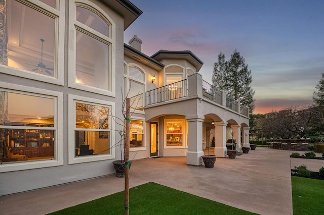 back house at dusk with a balcony and a patio area