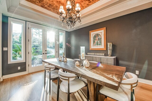 dining space with light wood-type flooring, ornamental molding, a raised ceiling, an inviting chandelier, and french doors