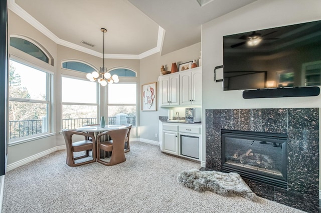 carpeted dining area featuring ornamental molding, sink, a tile fireplace, and a notable chandelier