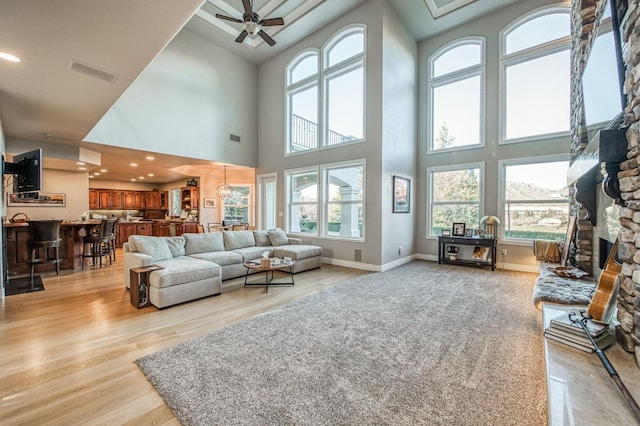 living room with a stone fireplace, light wood-type flooring, and ceiling fan