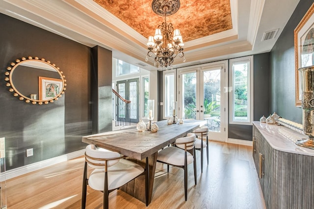 dining space with french doors, an inviting chandelier, ornamental molding, a tray ceiling, and light hardwood / wood-style floors