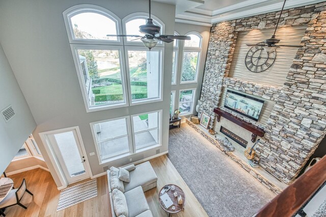 living room featuring ceiling fan, a stone fireplace, and light wood-type flooring