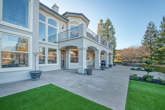 back of house with a balcony, a patio area, and a lawn