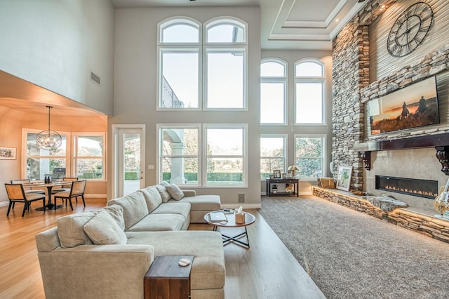 living room featuring a high ceiling, wood-type flooring, a stone fireplace, and an inviting chandelier