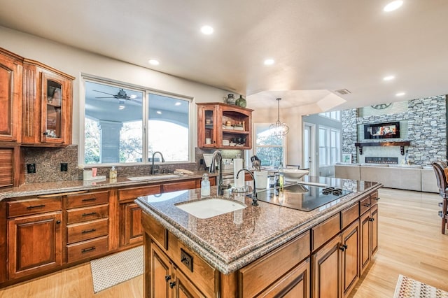 kitchen with sink, hanging light fixtures, a center island with sink, black electric stovetop, and backsplash