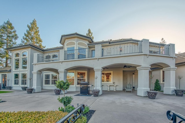 back house at dusk with a patio, a balcony, and ceiling fan