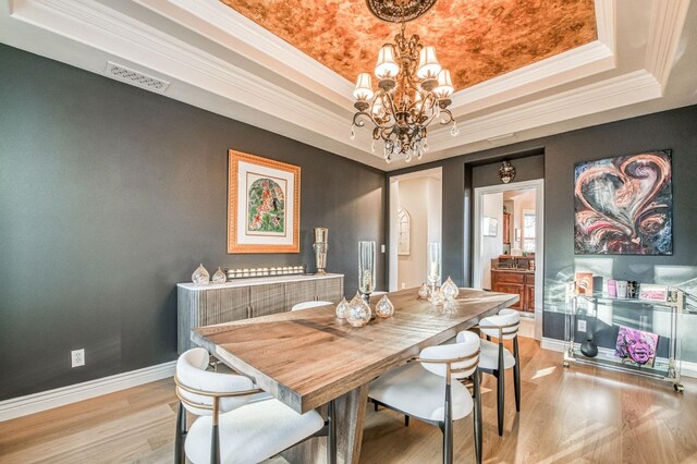 dining space featuring crown molding, a tray ceiling, a chandelier, and light hardwood / wood-style flooring