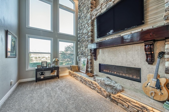 living room with a stone fireplace, a towering ceiling, and carpet