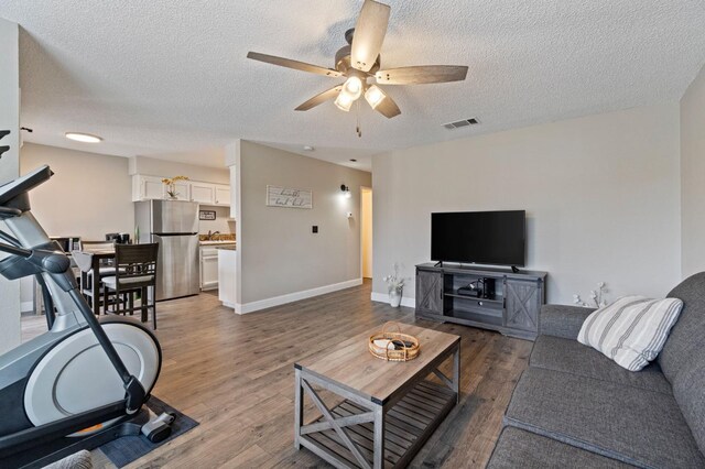 living room featuring dark wood-type flooring, ceiling fan, and a textured ceiling