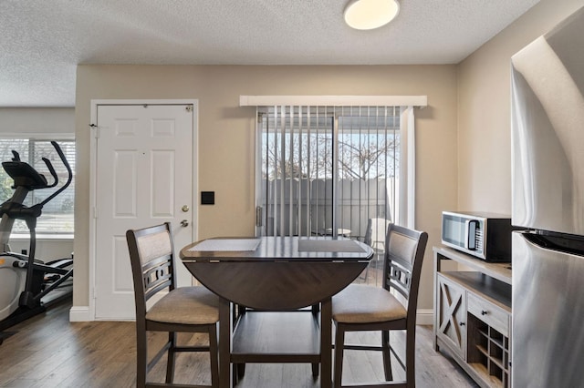 dining area featuring a textured ceiling, baseboards, and light wood-style floors