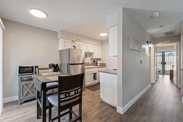 kitchen featuring visible vents, baseboards, appliances with stainless steel finishes, a textured ceiling, and light wood finished floors