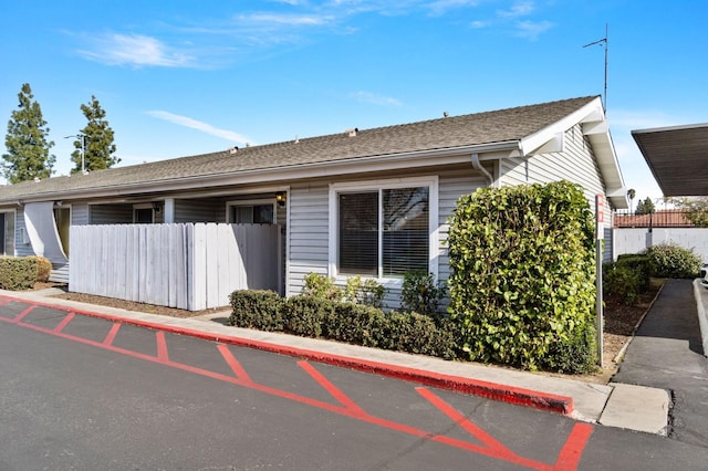 view of side of home featuring fence and a shingled roof