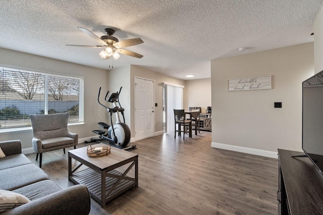 living area with ceiling fan, a textured ceiling, baseboards, and wood finished floors