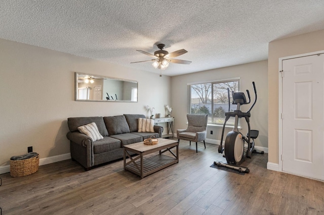 living area featuring a textured ceiling, baseboards, wood finished floors, and ceiling fan