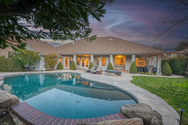 pool at dusk with french doors, a patio, and a lawn