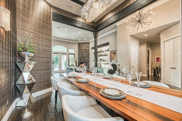 dining space featuring a stone fireplace, wood-type flooring, crown molding, an inviting chandelier, and french doors