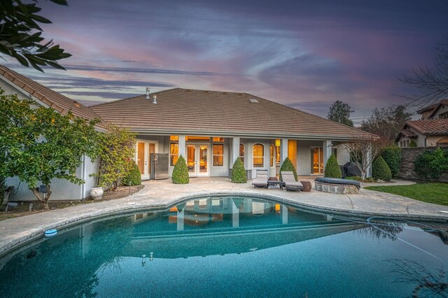 back house at dusk with a fenced in pool, a patio area, and french doors