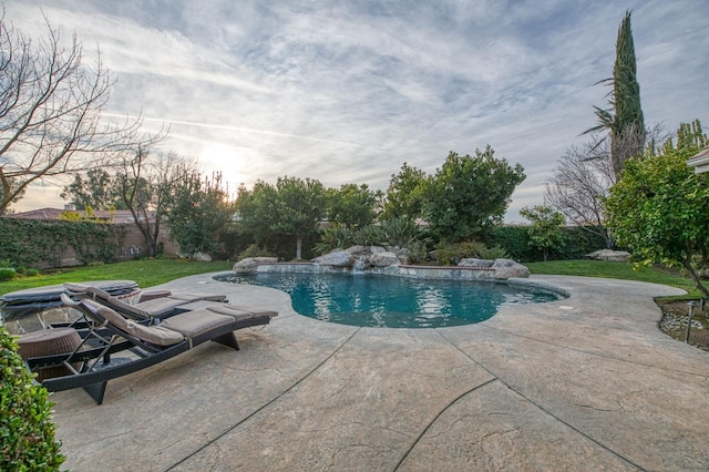 pool at dusk with pool water feature, a yard, and a patio