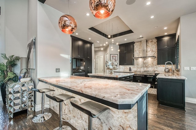 kitchen with dark wood-type flooring, wall chimney range hood, kitchen peninsula, and decorative light fixtures