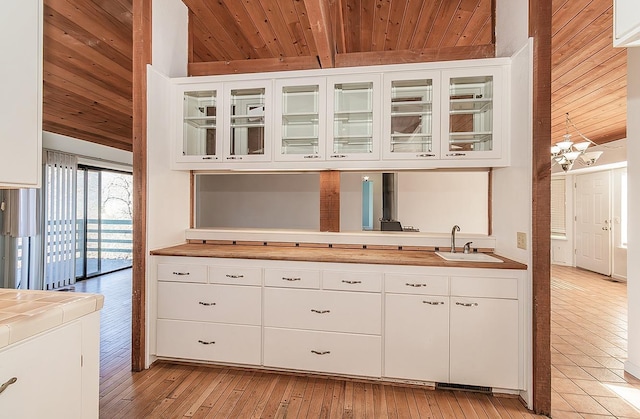 kitchen with white cabinetry, sink, wood ceiling, and an inviting chandelier