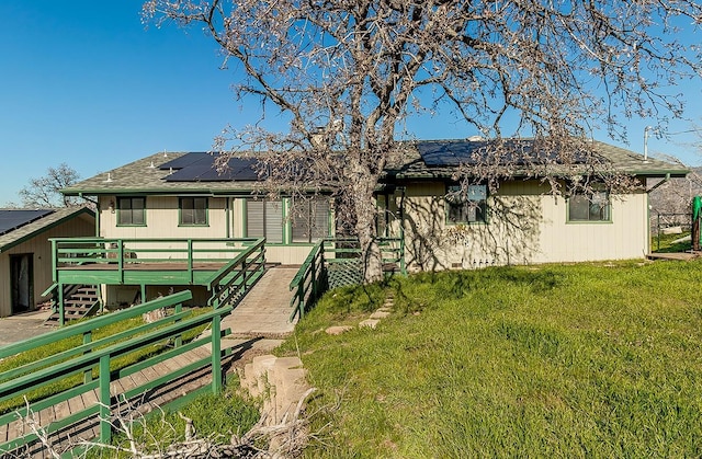 back of property with a wooden deck, a lawn, and solar panels