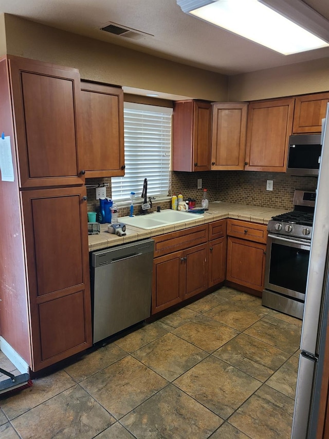 kitchen with appliances with stainless steel finishes, tile countertops, sink, and backsplash