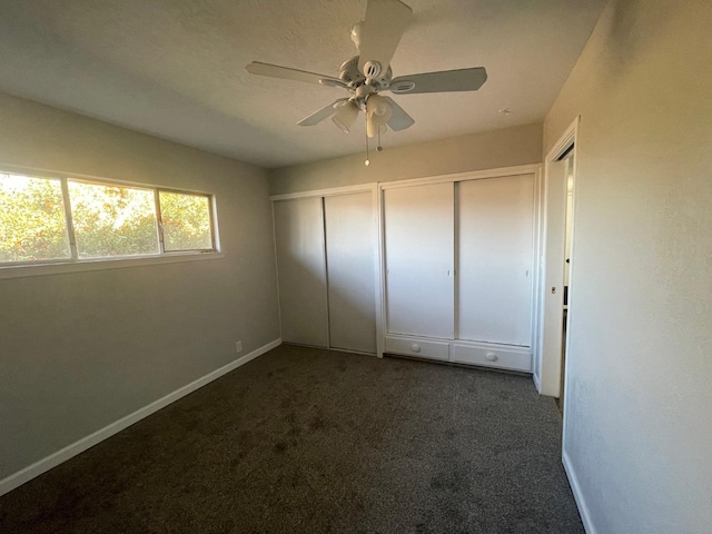 unfurnished bedroom featuring multiple closets, ceiling fan, and dark colored carpet