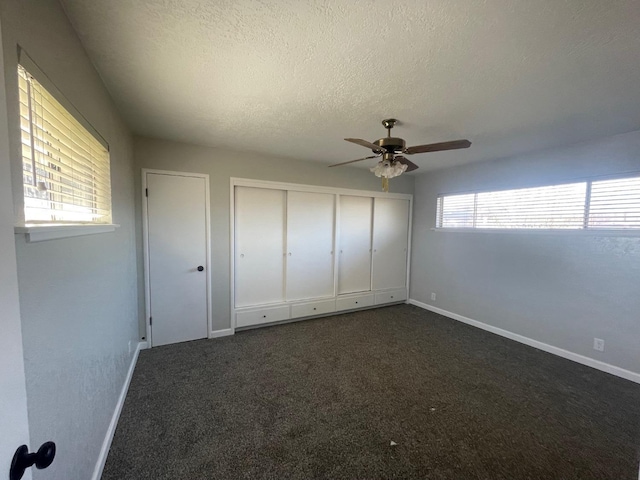 unfurnished bedroom featuring dark colored carpet, a textured ceiling, ceiling fan, and a closet