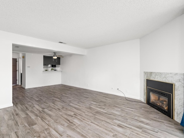 unfurnished living room featuring ceiling fan, a fireplace, hardwood / wood-style floors, and a textured ceiling