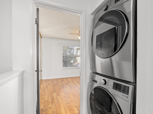 laundry room featuring ceiling fan, wood-type flooring, stacked washing maching and dryer, and a textured ceiling