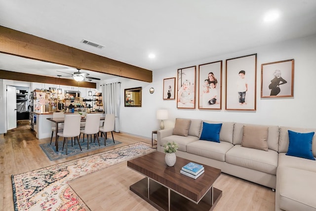 living room featuring beam ceiling, ceiling fan, and light wood-type flooring