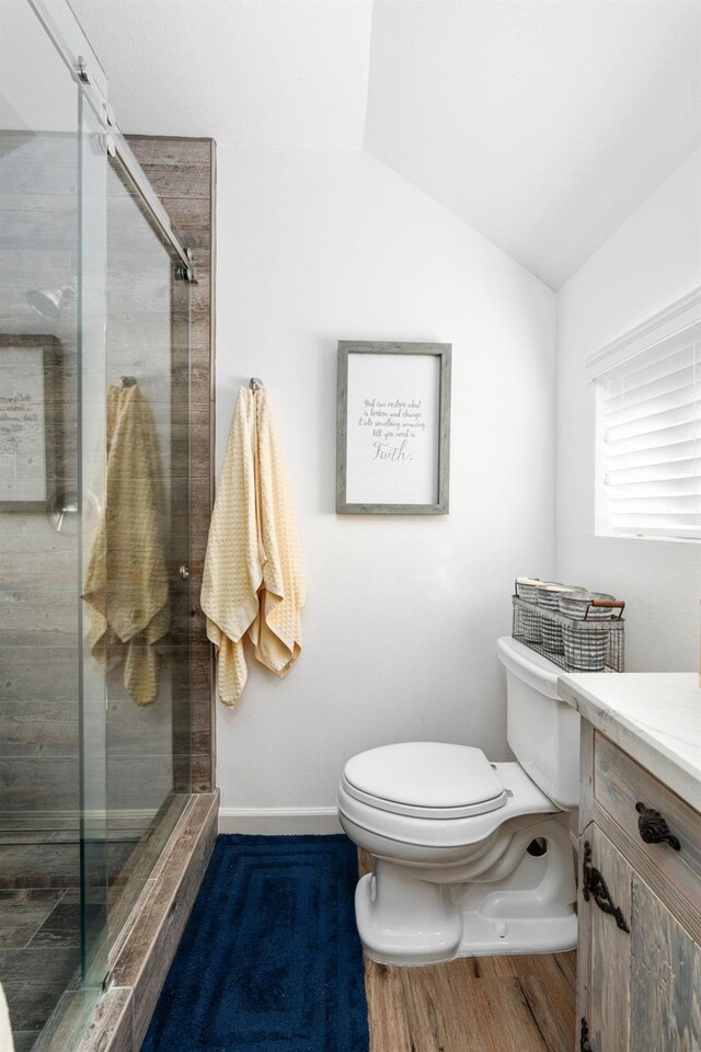 bathroom with vanity, toilet, a shower with door, and vaulted ceiling