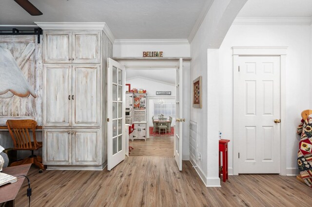 hallway with crown molding, lofted ceiling, and light wood-type flooring