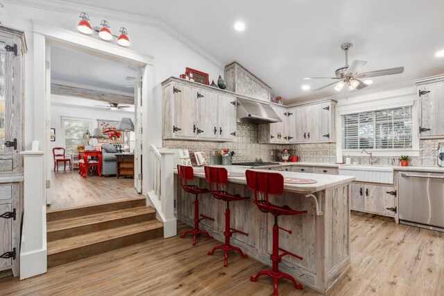 kitchen with lofted ceiling, sink, ventilation hood, stainless steel dishwasher, and ornamental molding