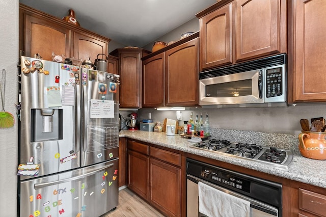 kitchen with appliances with stainless steel finishes, light stone countertops, and light hardwood / wood-style flooring