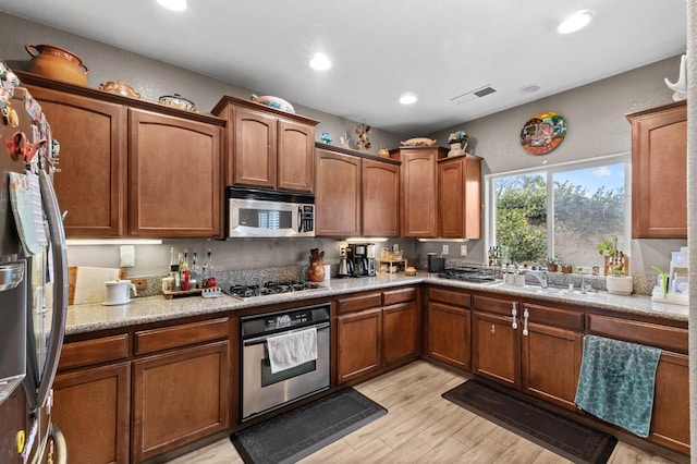 kitchen with stainless steel appliances, sink, light stone counters, and light hardwood / wood-style flooring