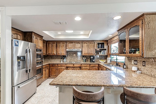 kitchen with appliances with stainless steel finishes, a tray ceiling, a kitchen breakfast bar, decorative backsplash, and kitchen peninsula