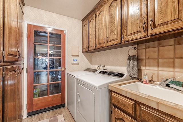 clothes washing area with cabinets, washer and dryer, sink, and light hardwood / wood-style flooring