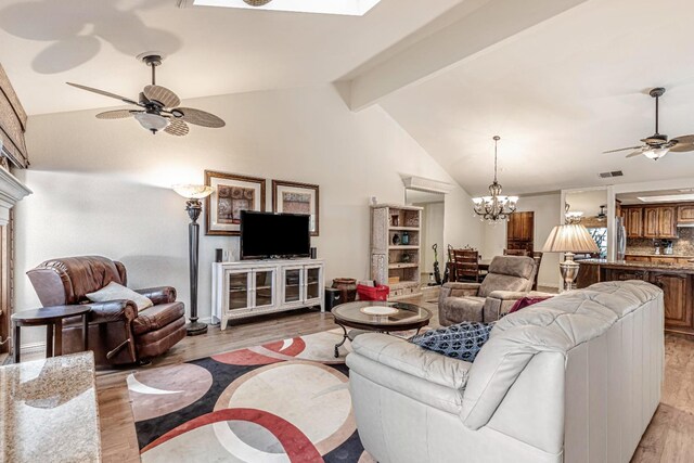 living room featuring ceiling fan with notable chandelier, lofted ceiling with beams, and light wood-type flooring