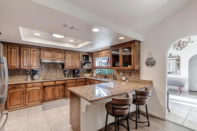 kitchen featuring sink, black electric cooktop, a tray ceiling, kitchen peninsula, and backsplash